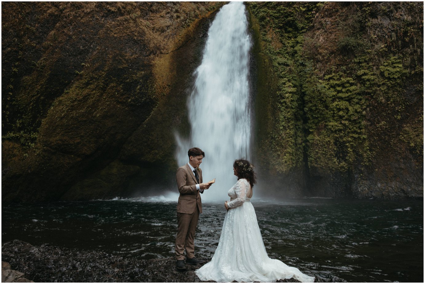 Wedding couple stand on rocks at the bottom of Wahclella falls while exchanging their vows