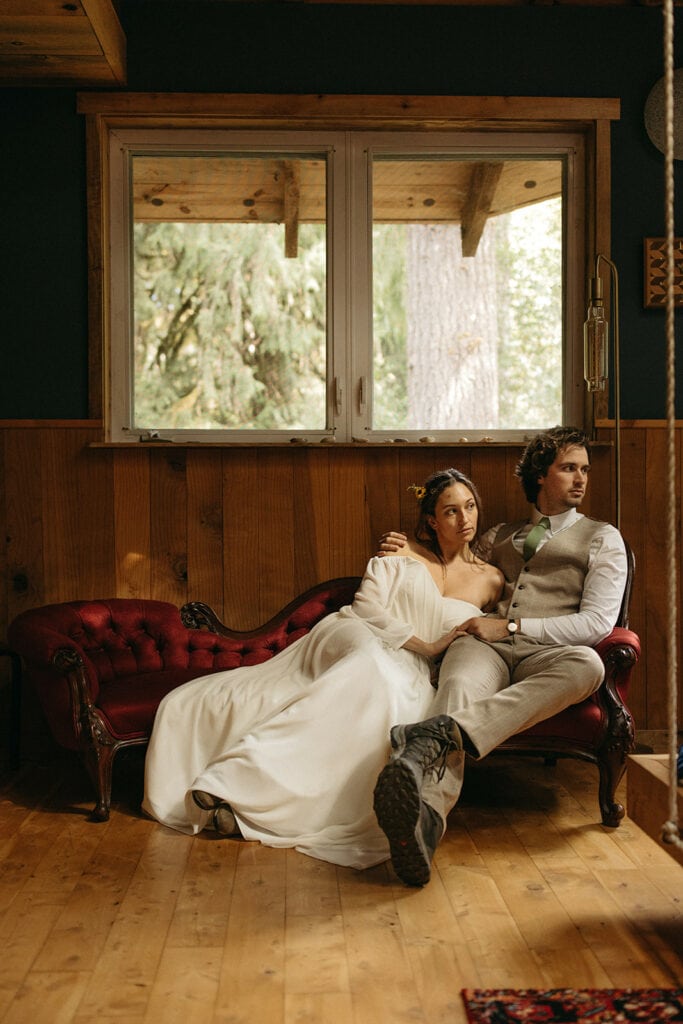 bride and groom posed shot grooms arm around bride sitting on red couch staring away 