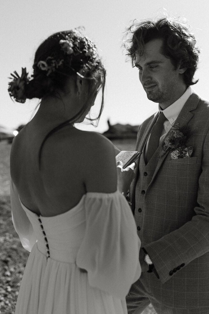 black and white shot bride reading vows to groom while grooms smiles at bride 