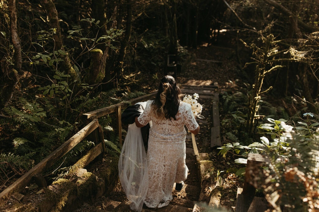 bride walking down a wooden staircase through a forest to the beach