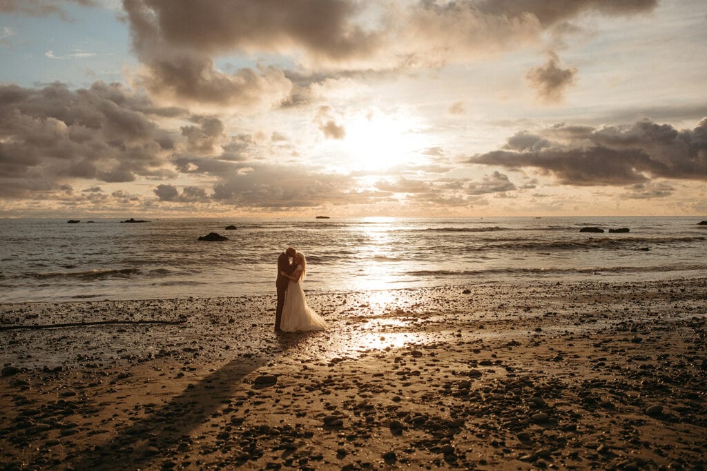 man and woman standing on the beach kissing during golden hour