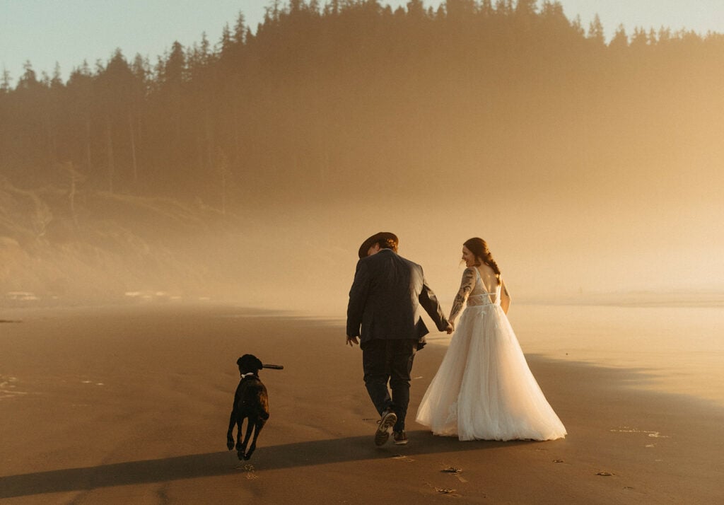 elopement shot of bride and groom walking along the beach with their dog 