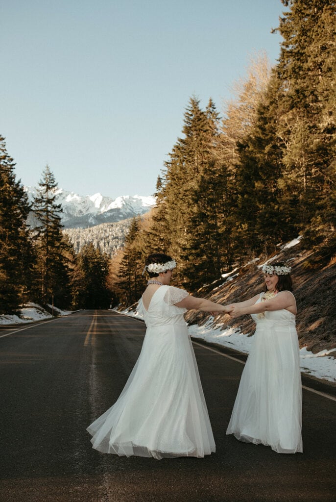 bride and bride holding hands and smiling at each other in the middle of the road after elopement