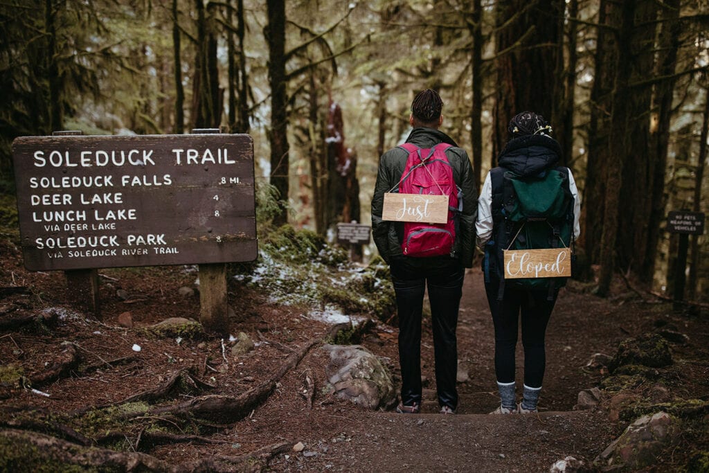 couple backpacks walking to Sol Duc Falls with the signs "just eloped" on their backs 
