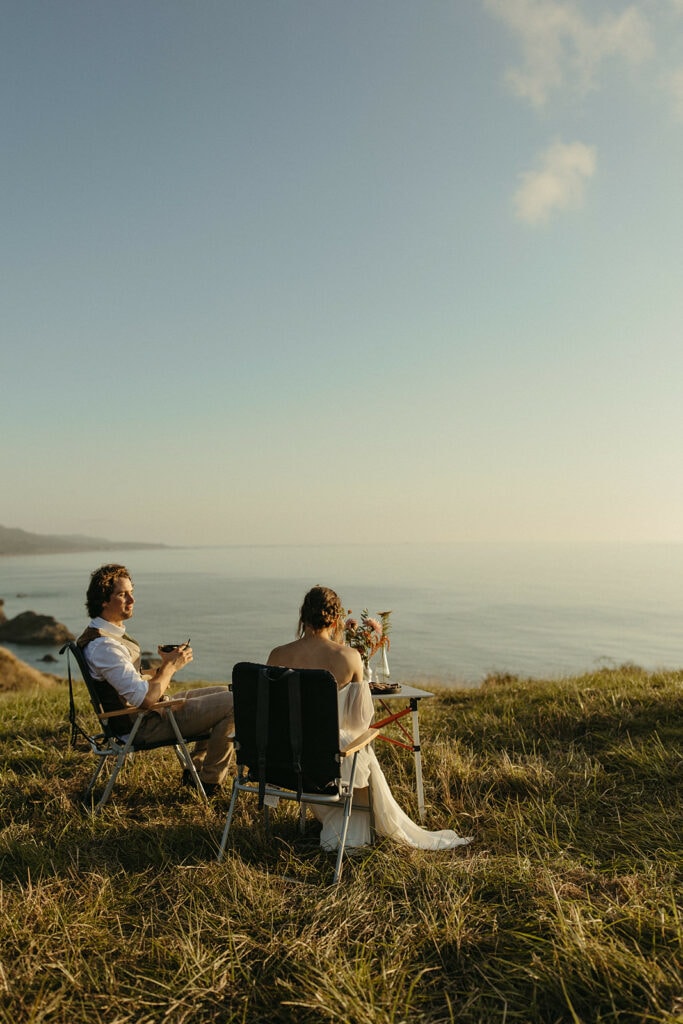 bride and groom eat a meal at sunset on a cliffside on Oregon Coast