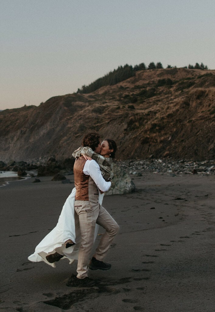 groom carrying bride along the sand on the Oregon Coast