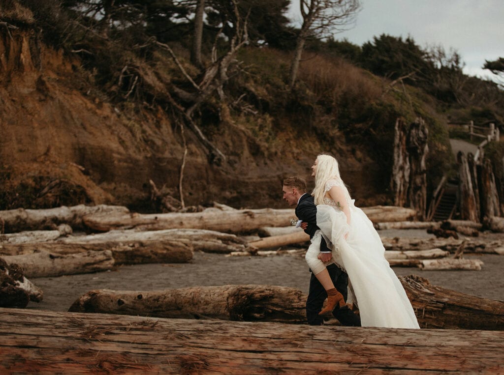 Groom carries bride piggy back style along the sand at Kalaloch Beach
