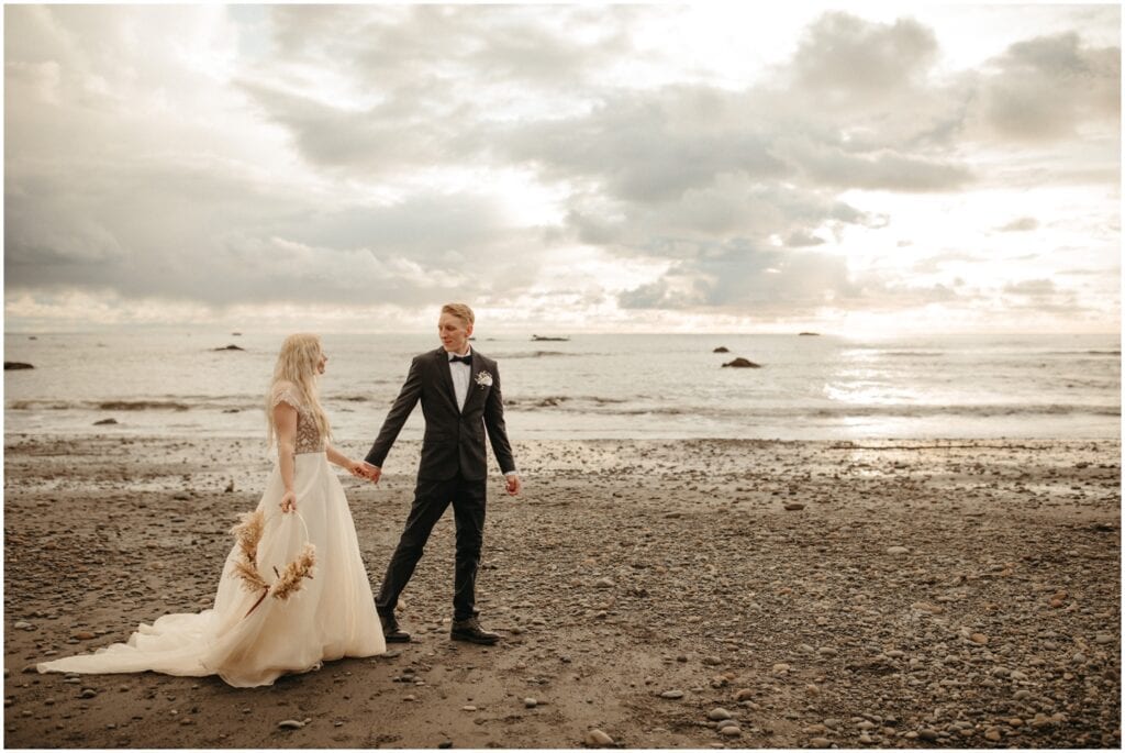bride and groom standing on the sand walking and staring at each other at Ruby beach in Washington state