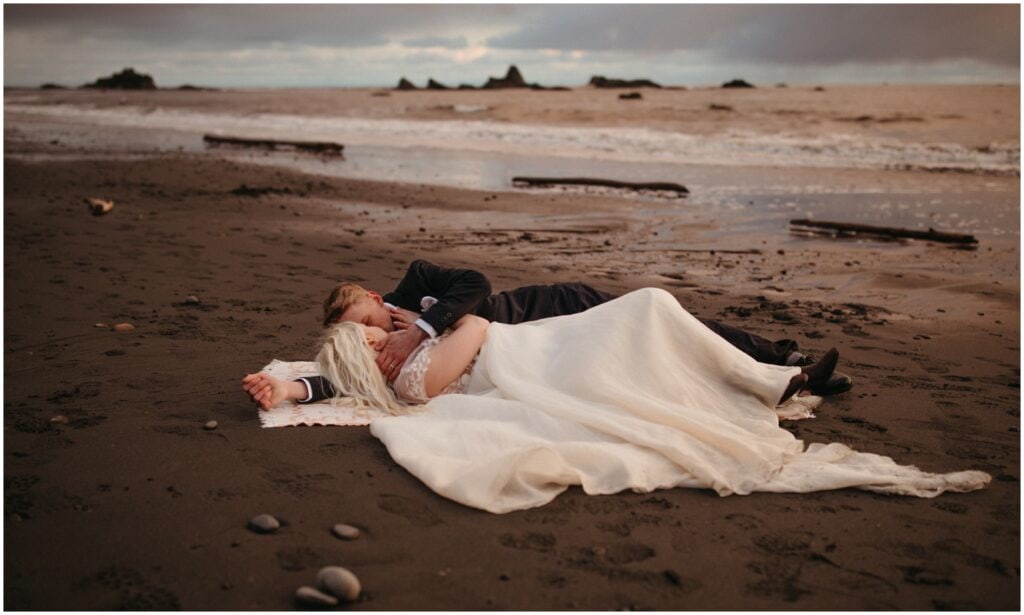 bride and groom laying on the sand with their faces close to each other at ruby beach in Washington state