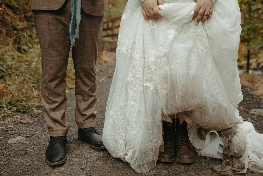 man and woman standing side by side as she lifts up her dirty wedding dress
