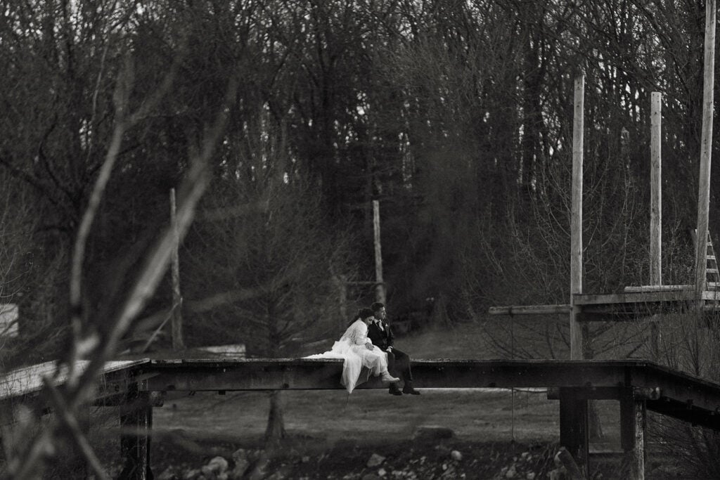 couple sitting on a wooden bridge in the distance