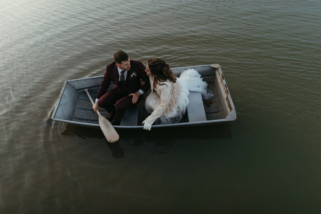 bride and groom sitting in a metal boat in the middle of the pond