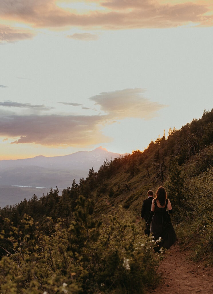 couple walking down a mountain trail with a scenic view in front of them