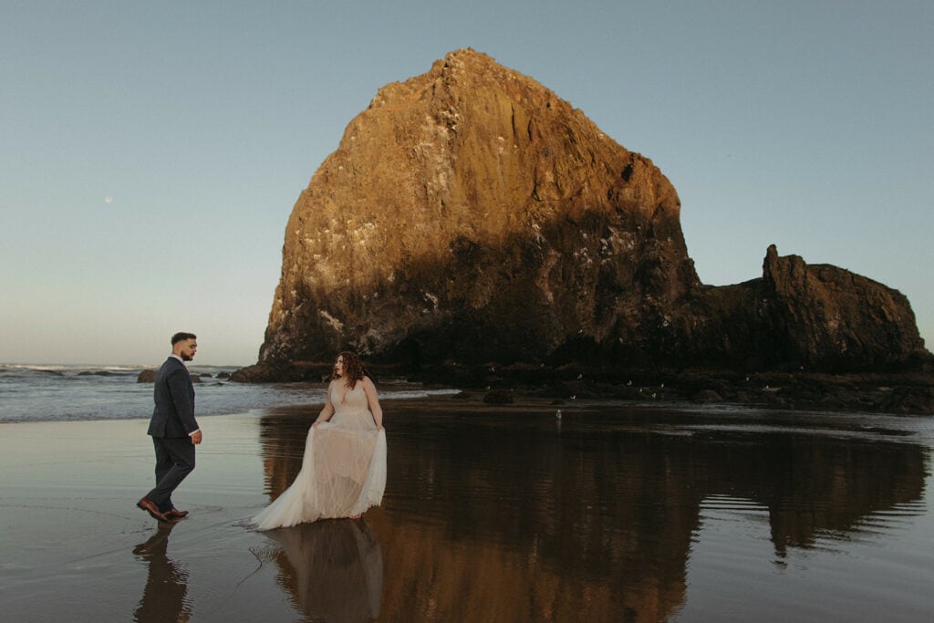 A newly married couple running around Cannon Beach in front of Haystack Rock.