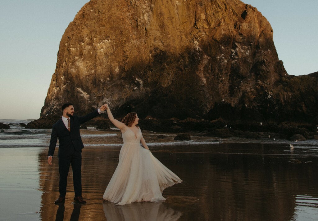 A newly married couple running around Cannon Beach in front of Haystack Rock.