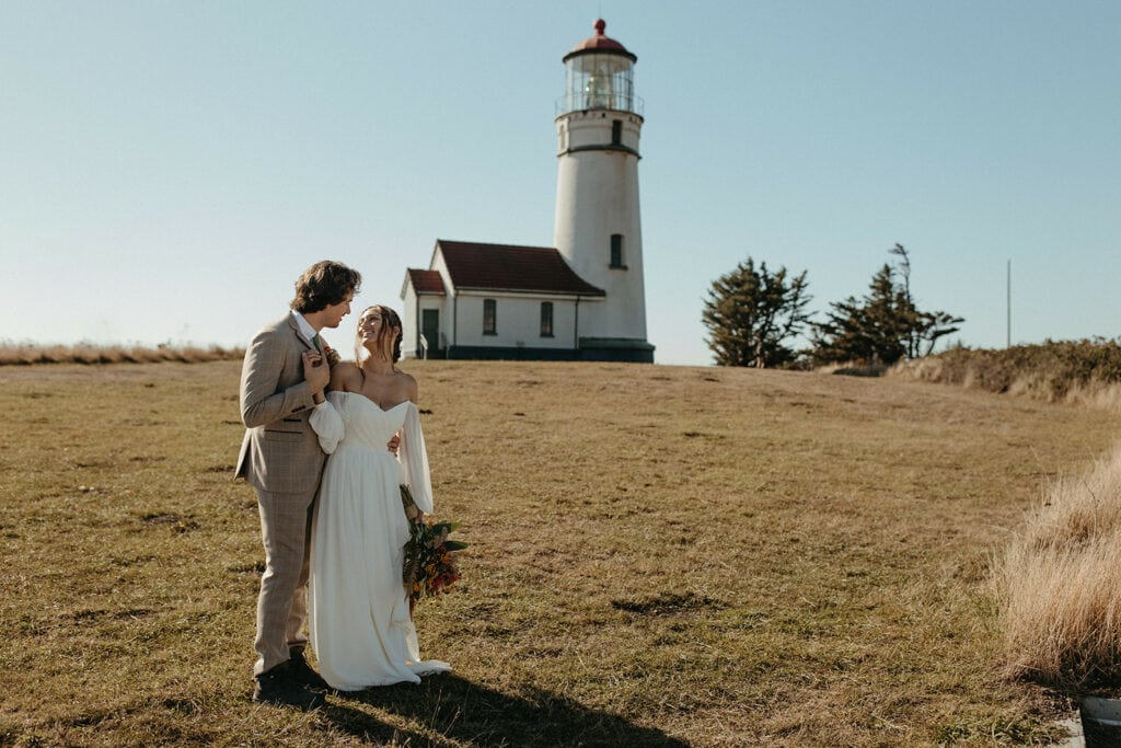 an elopement couple stands together with an Oregon lighthouse in the distance