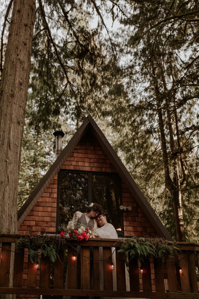 A couple stands on the balcony of a forest Airbnb before their ceremony