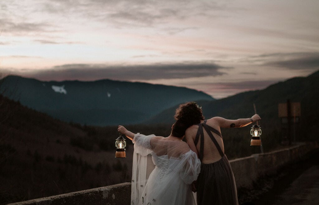 A couple stands on a Mt. Hood viewpoint holding lanterns after sunset