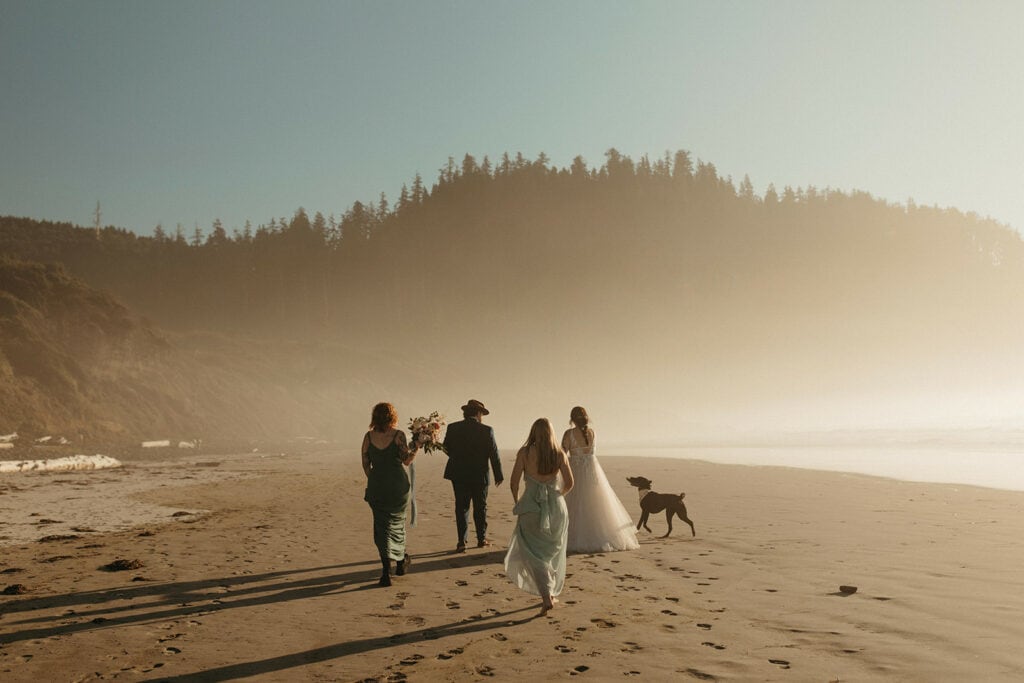 Bride and groom walking down to Cape Meares beach with family and friends